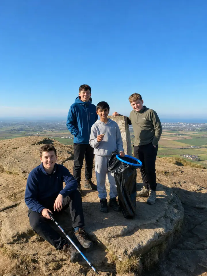Students at a hilltop trig point during a litter pick
